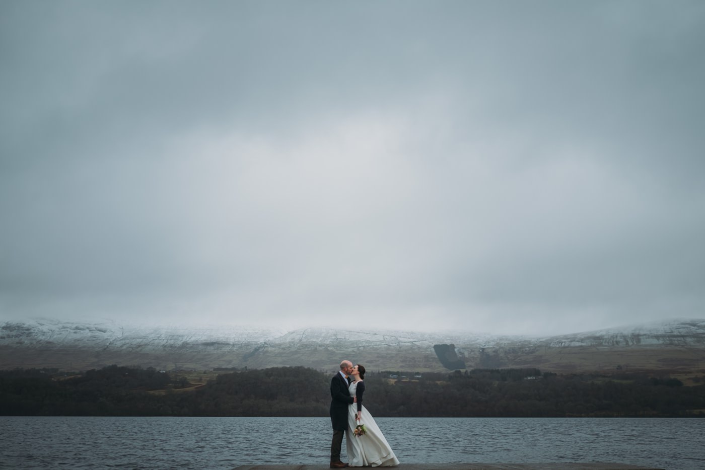 A newly married couple kiss at Ardenoaig, Loch Tay in the background on their scottish elopement.