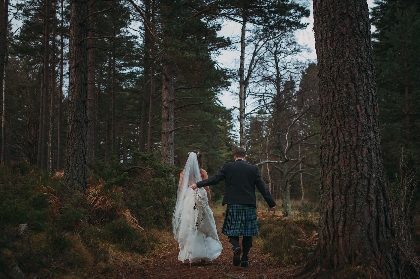 groom holds bride dress so they can walk during their Christmas wedding at Glen Tanar