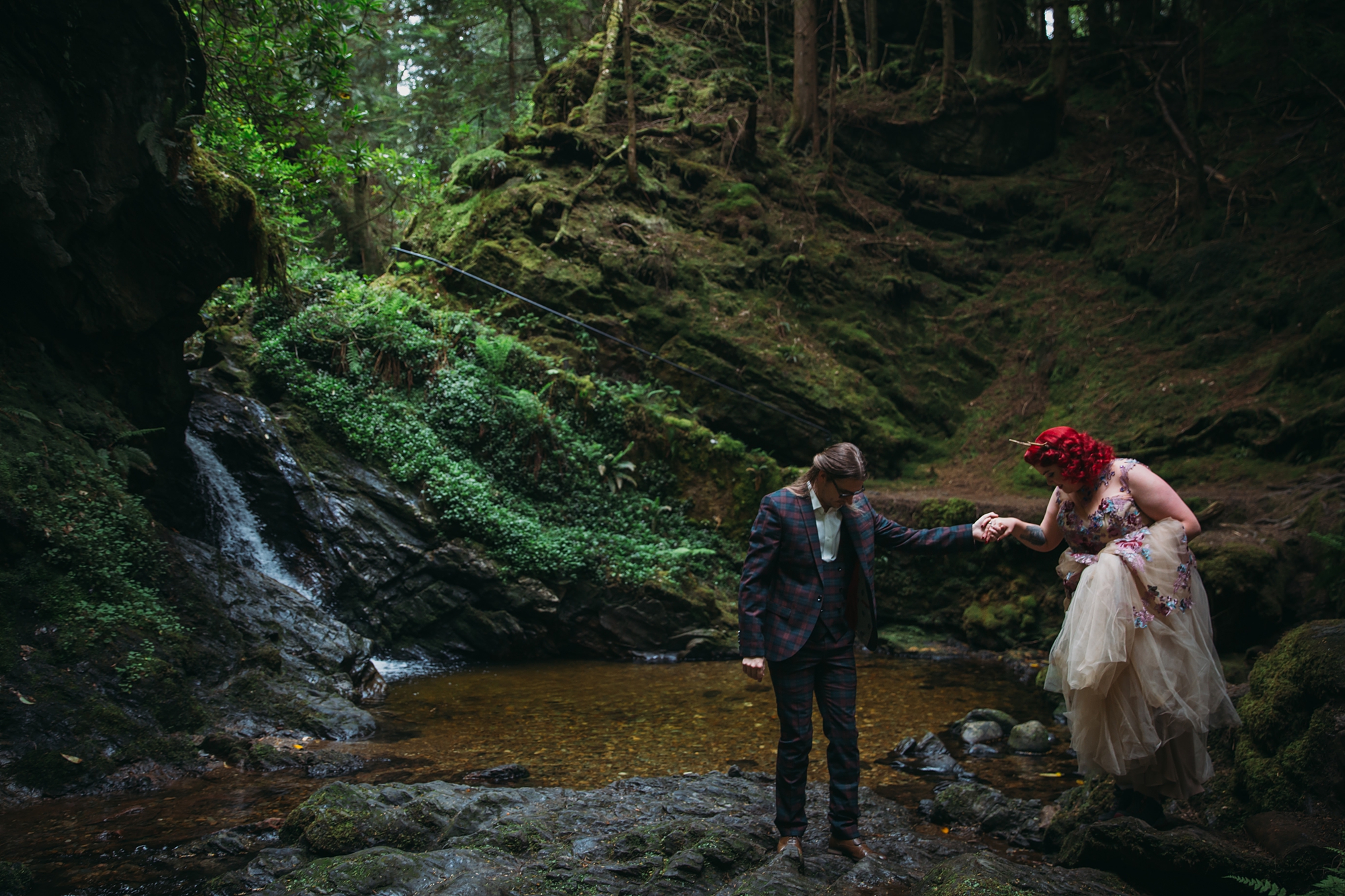best wedding photographs of a groom helping his bride down to a waterfall