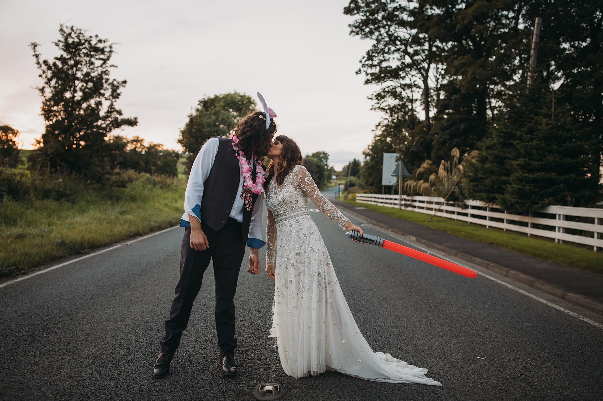 a crazy coupe kiss on a road, she is holding a lightsaber! best wedding photographs