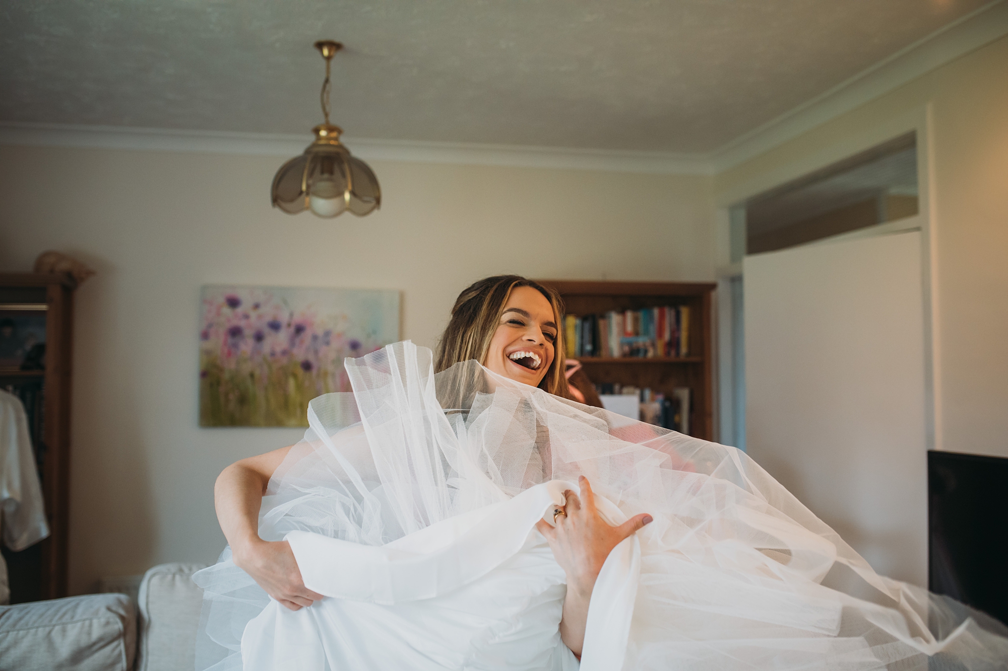 best wedding photographs of sister helping the bride get ready, laughing at size of dress