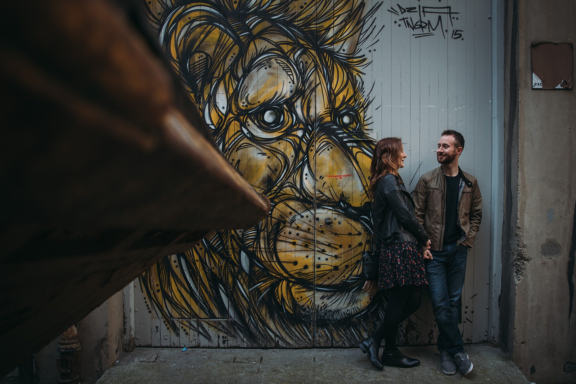 Couple stand next to graffiti of a lion on their Glasgow engagement photography in the Merchant City