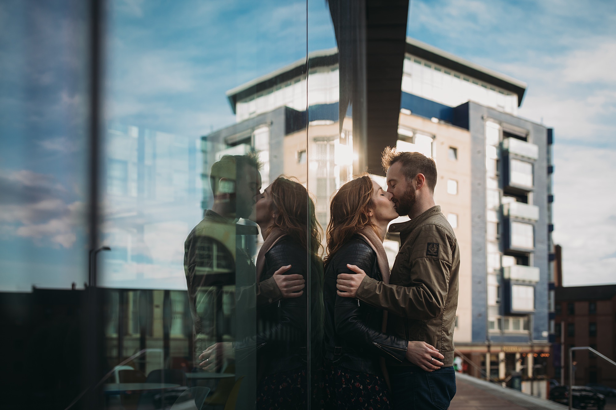 A couple kiss, reflected on the window behind them during their Glasgow engagement
