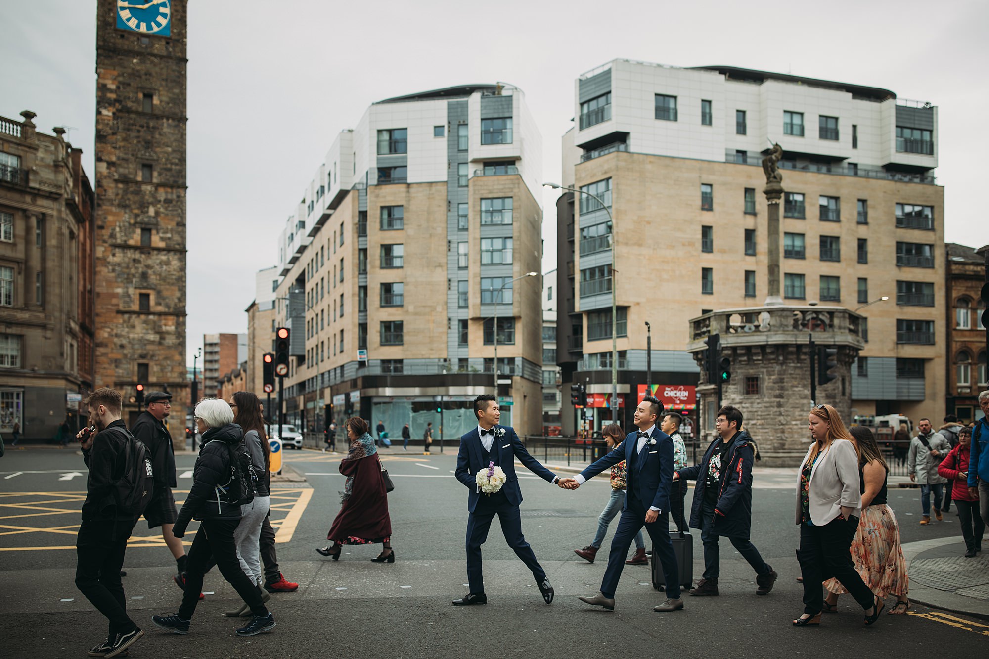 Two grooms walk amongst the crowds during their Glasgow elopement.
