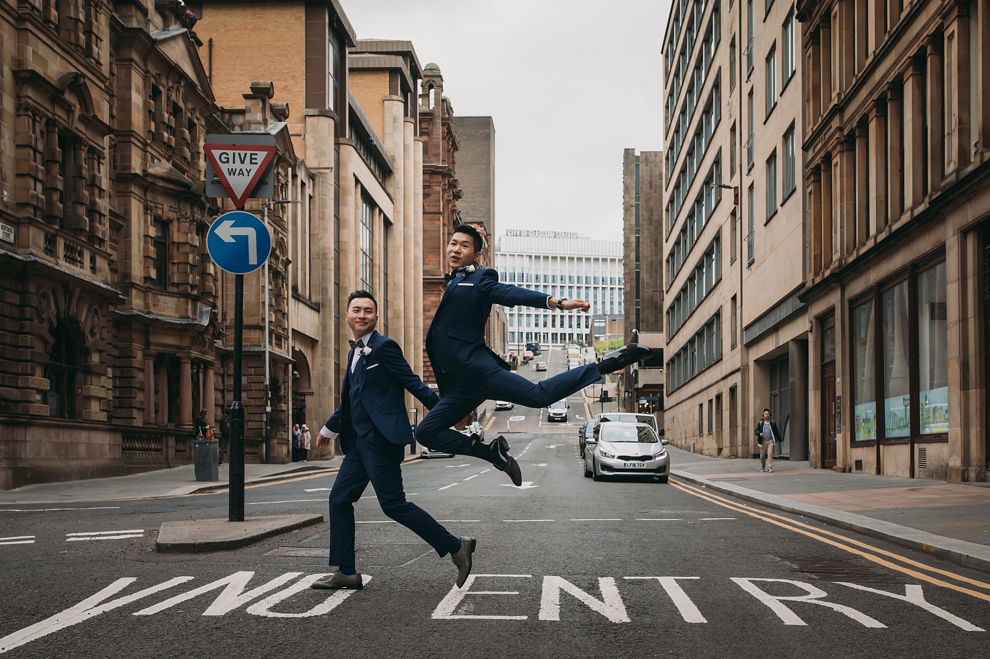 Two grooms cross the street during their Glasgow elopement. One of the grooms is a dancer and leaps into the air in celebration!