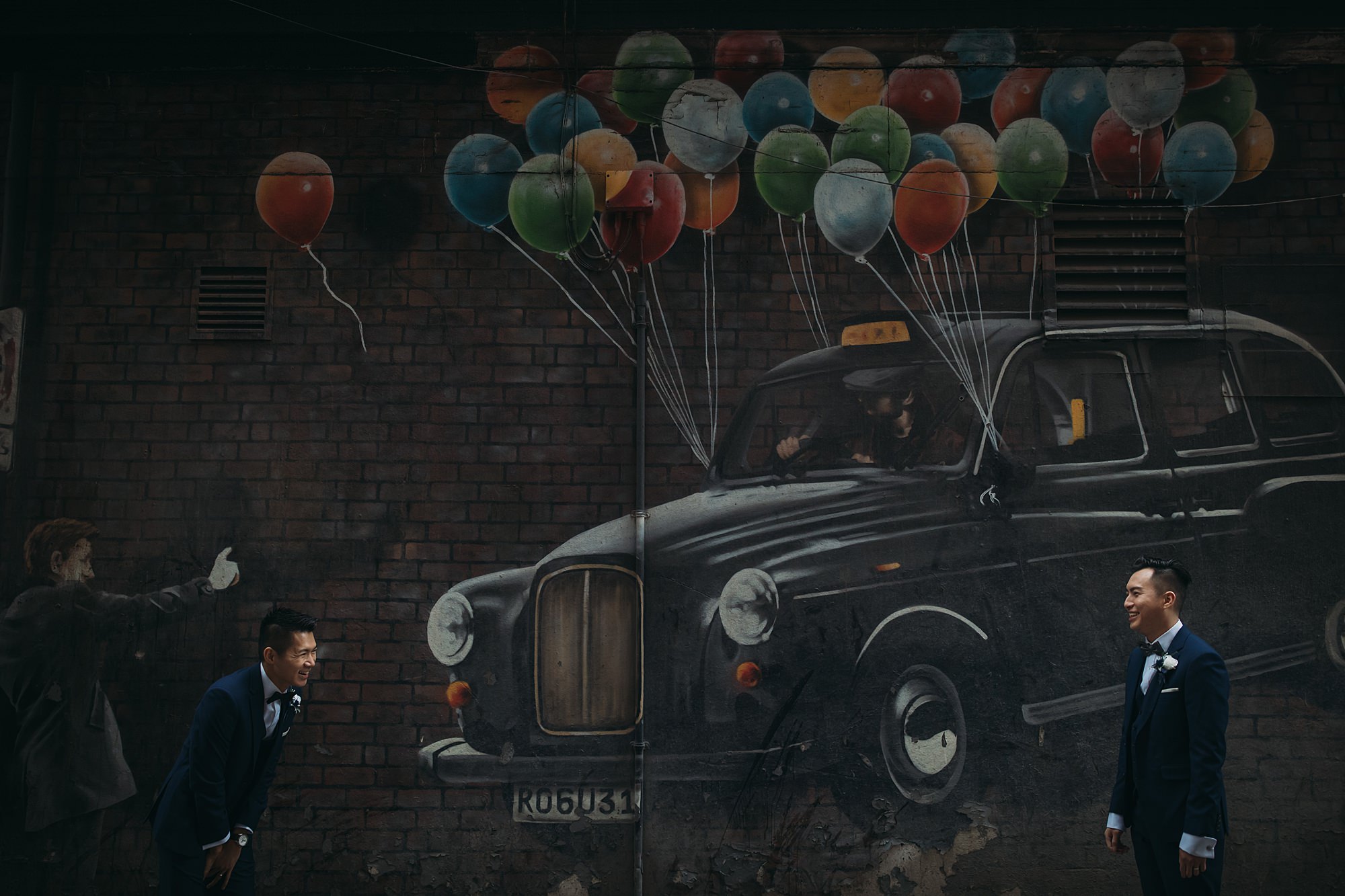Two grooms laugh together in front of Rogue 1 graffiti during their Glasgow elopement.