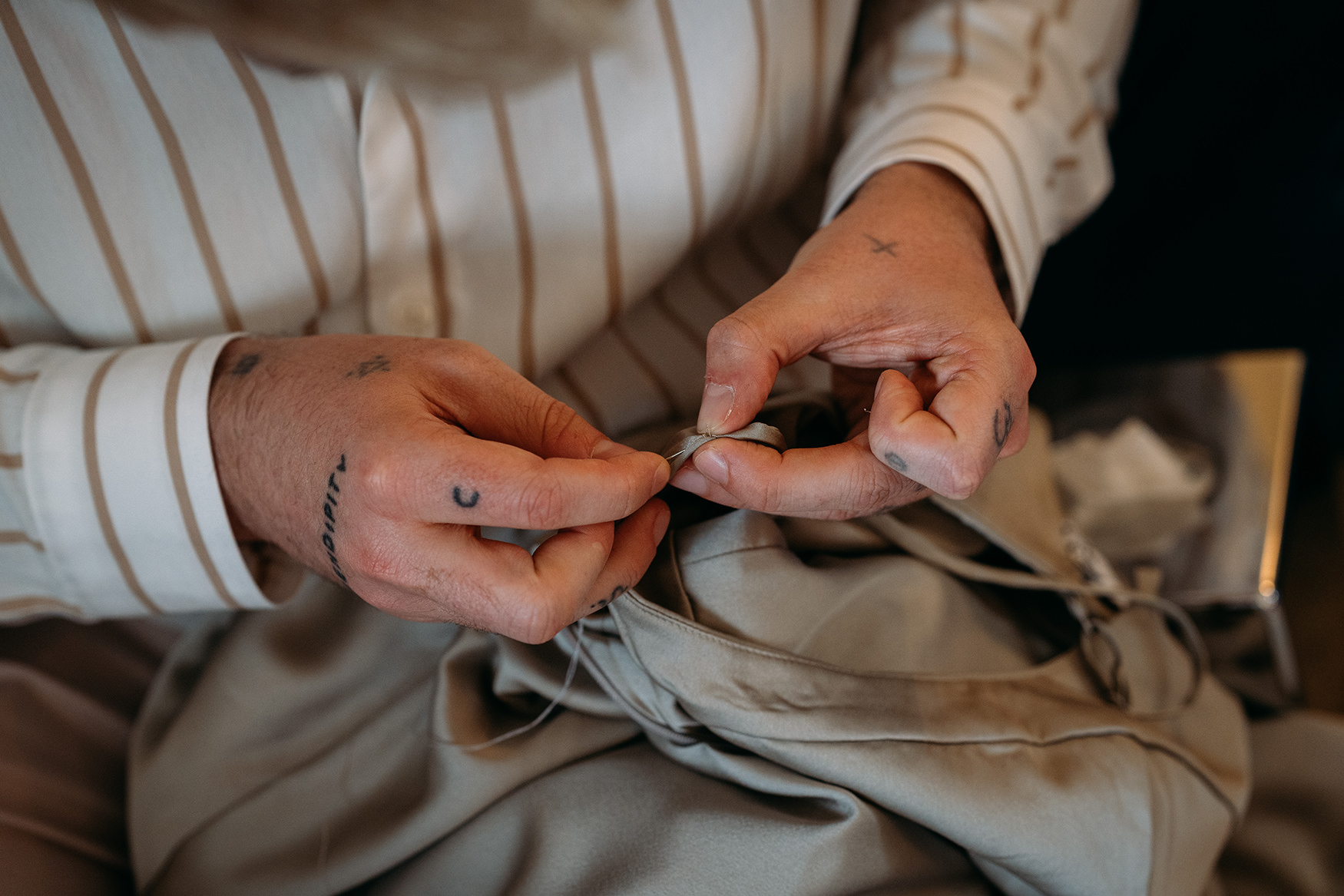 Tattooed hands stitching broken bridesmaid dress on wedding morning using wedding day emergency kit
