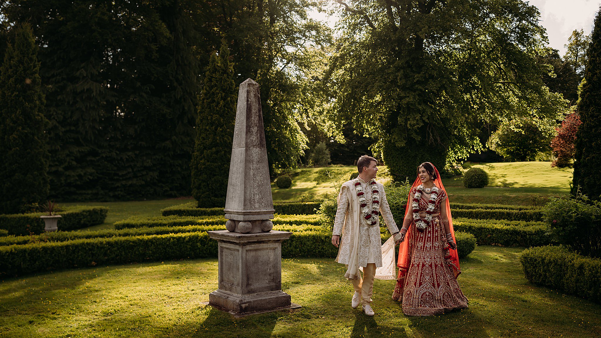 Newlyweds walk together through gardens during their Indo-Scottish Achnagairn Castle wedding