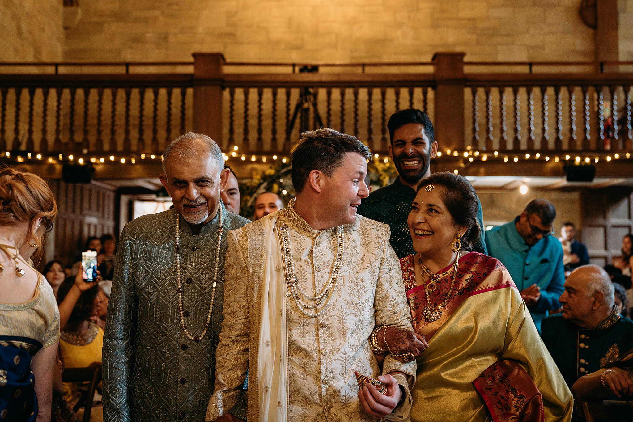 Groom shares look with Brides Mum, both laughing as his shoes have just been stolen at his Indo-Scottish Achnagairn Castle wedding