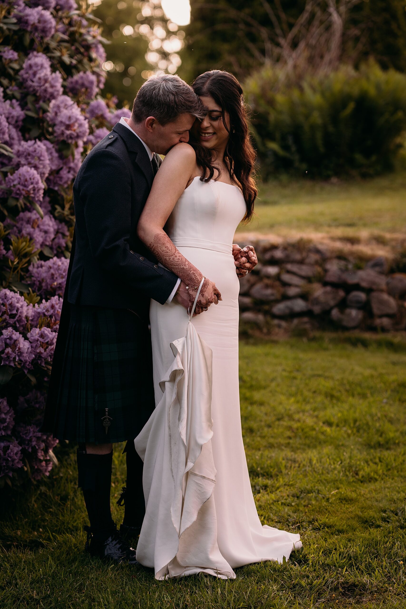 Groom kisses brides shoulder during golden hour at Indo-Scottish Achnagairn Castle wedding