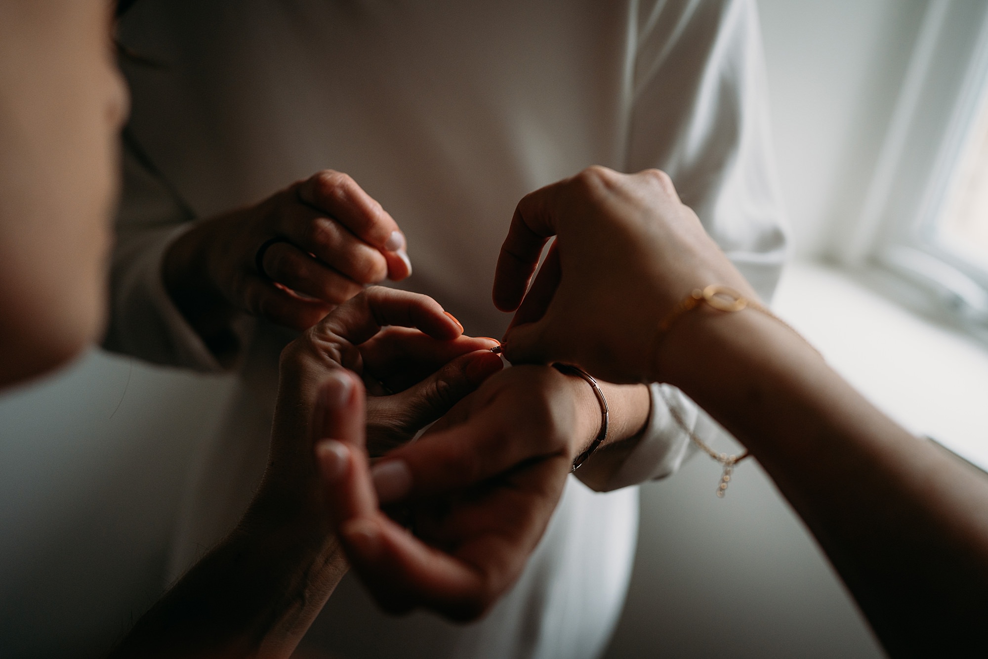 Closeup of hands helping a bride put her bracelet on. Relaxed wedding photography in Braemar with Coorie Wedding Planning