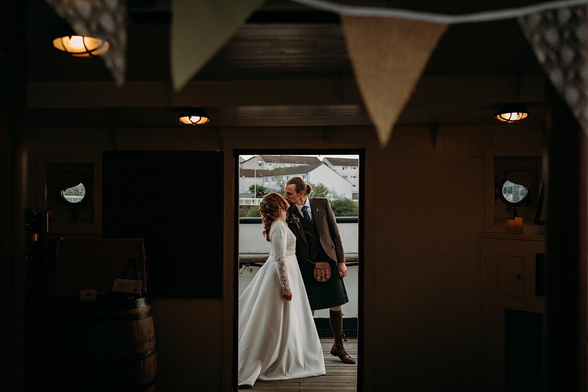 Newlyweds kiss at their Glasgow wedding. The photograph is taken through a doorway creating a natural frame. Relaxed wedding photography on the Tall Ships.