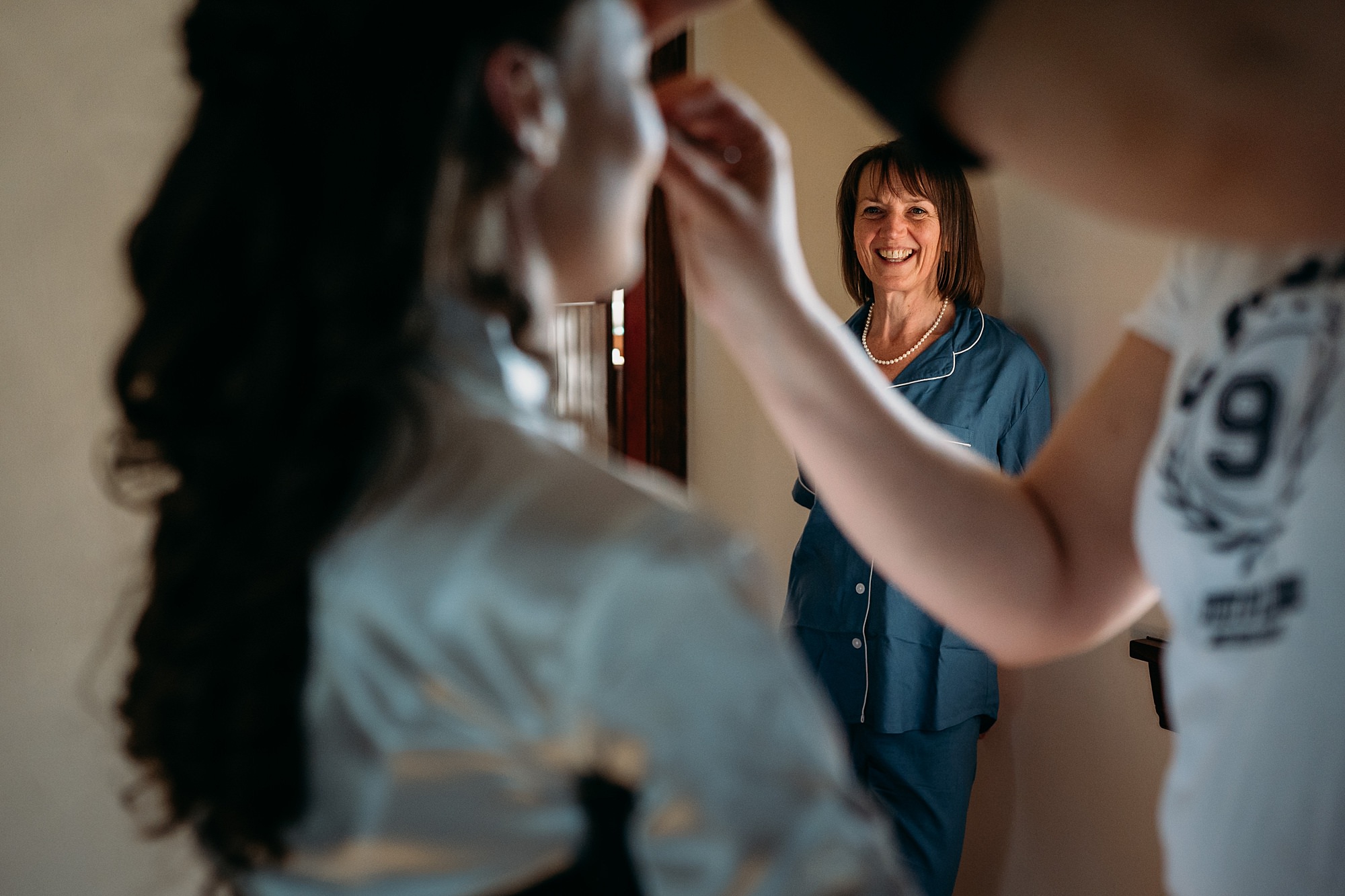 Mum looks at daughter with love as she has her makeup done. Relaxed wedding photography at harelaw Farm Ayrshire.