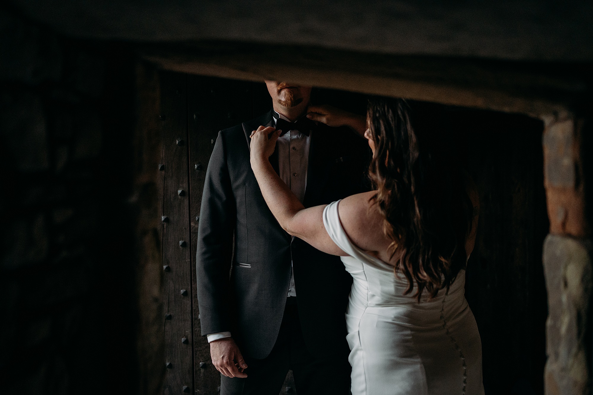 Bride straightens grooms tie. Couple are framed in doorway, which cuts off top half of grooms head. relaxed wedding photography at Rowallan Castle