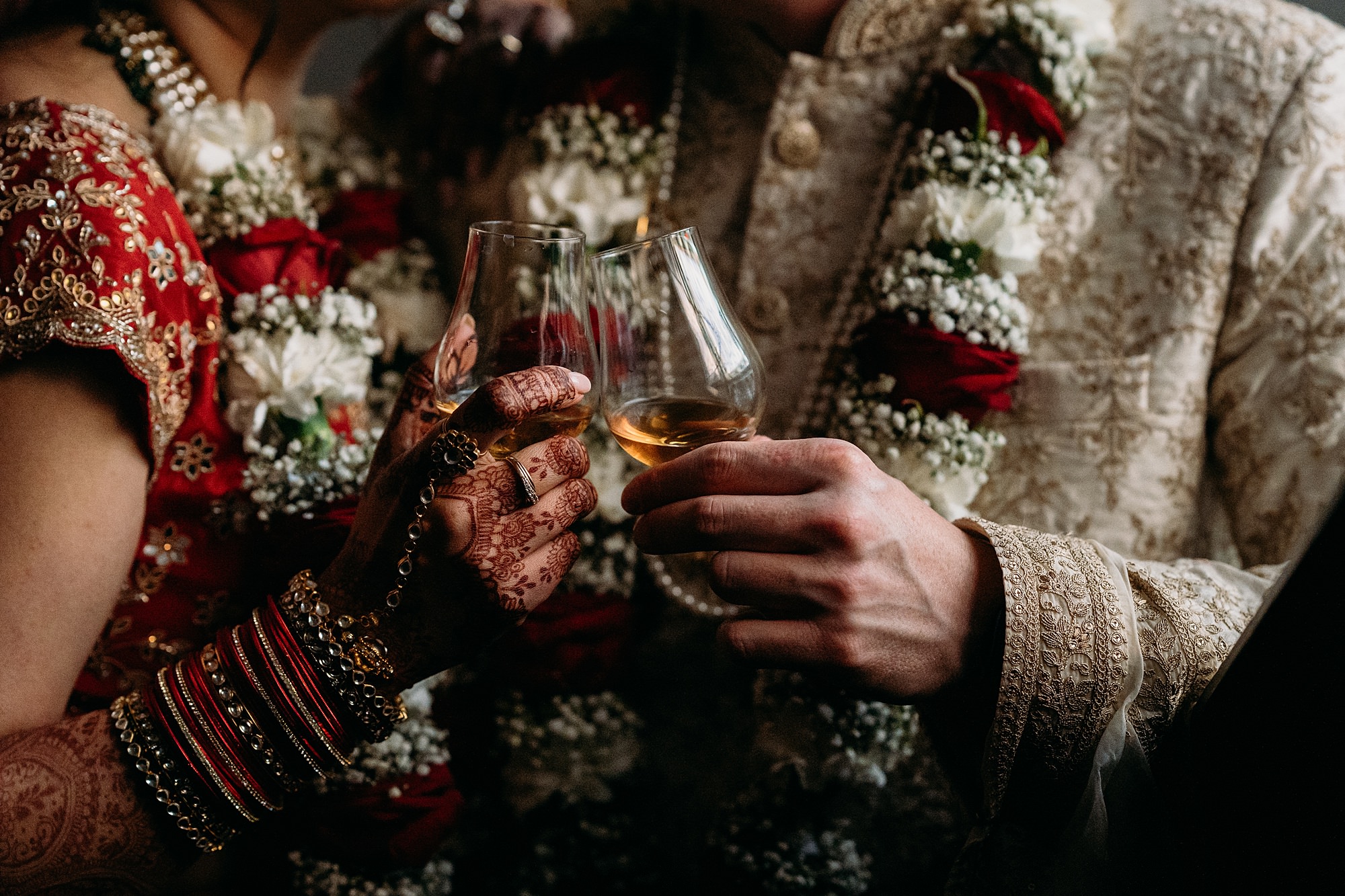 two hands holding whisky glasses. The bride has henna on her hands. relaxed wedding photography at Achnagairn Castle.