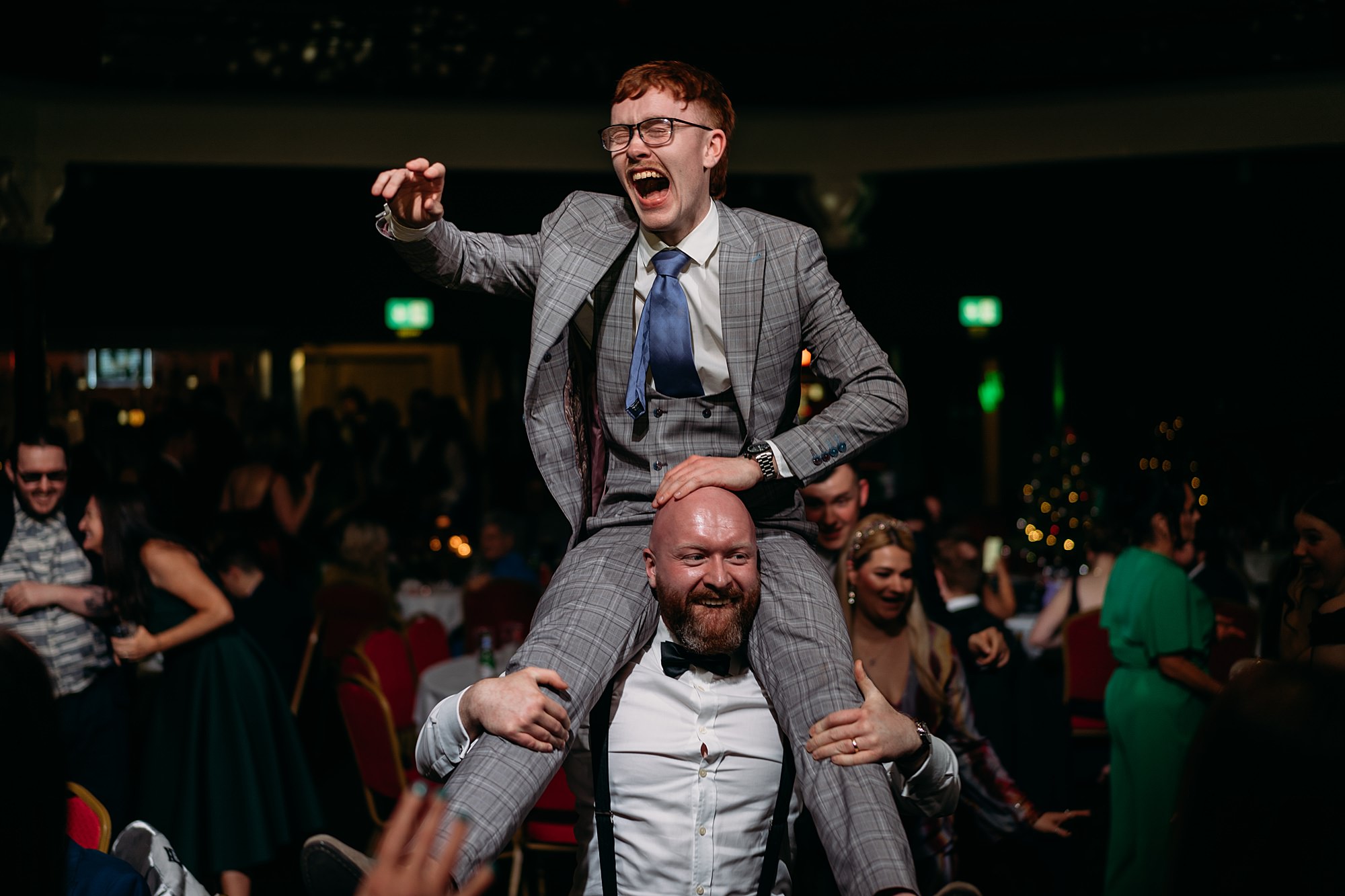 Man laughs as he is lifted onto another mans shoulders during wedding party. relaxed wedding photography at St Lukes Glasgow