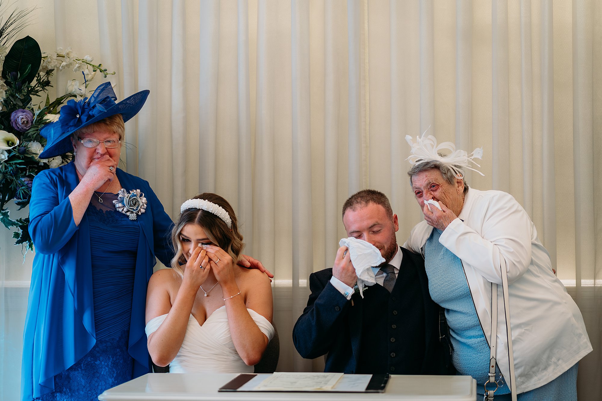 Bride and groom have surprised their grans by asking them to sign their register. All four of them are wiping happy tears from their eyes. Relaxed wedding photography at Montrose Street Glasgow.