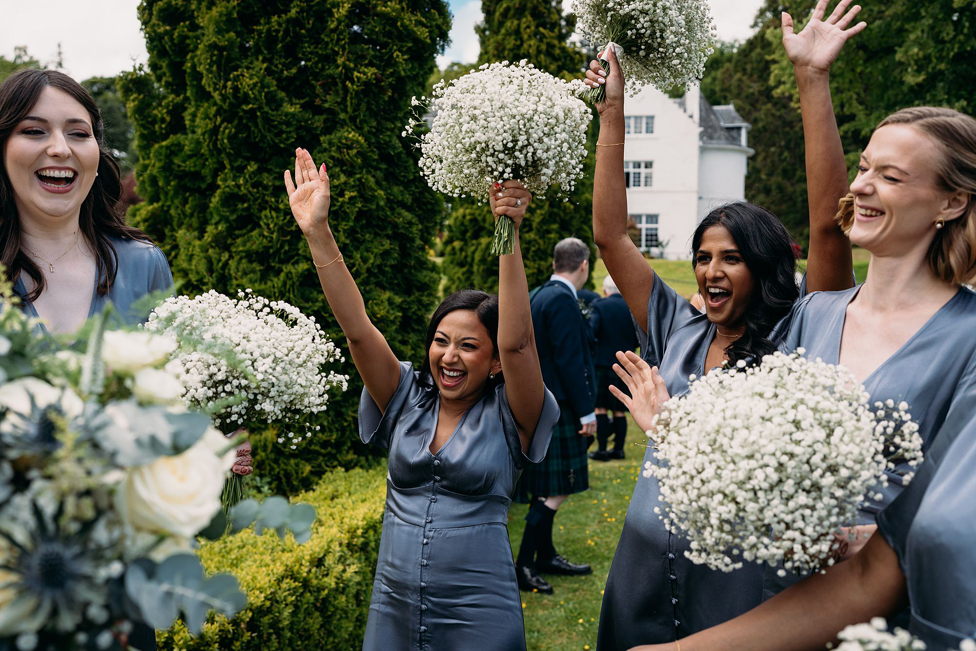 Bridesmaids celebrate the happy couple, their arms raised joyfully. Relaxed wedding photography at Achnagairn Castle.