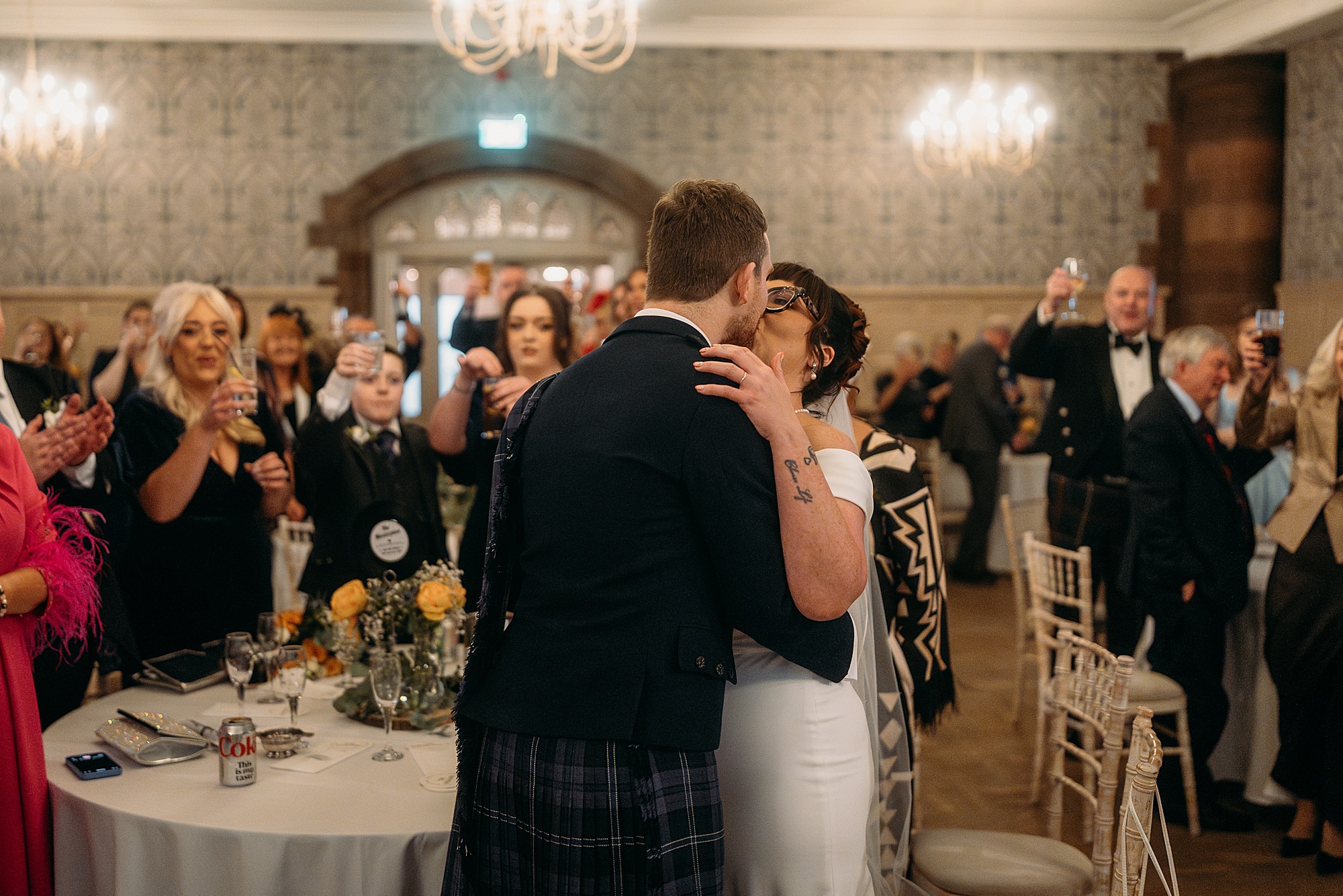 Newlyweds kiss as their guests cheer and clap at a Coats Paisley Twilight Wedding