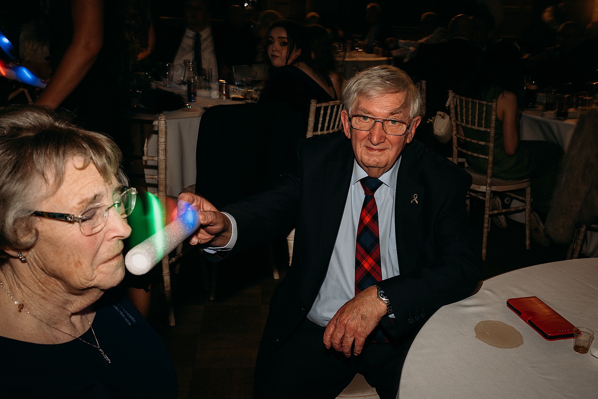male guest tickles wifes nose with glow stick at Coats Paisley Twilight Wedding party